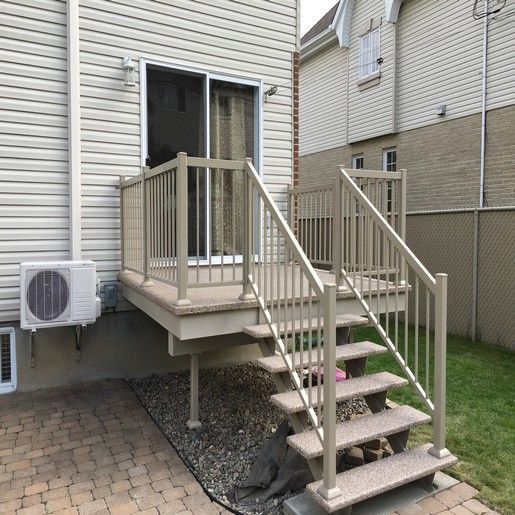 Terrasse beige avec escalier et rambarde à l'extérieur d'une maison avec porte-fenêtre coulissante et climatiseur.