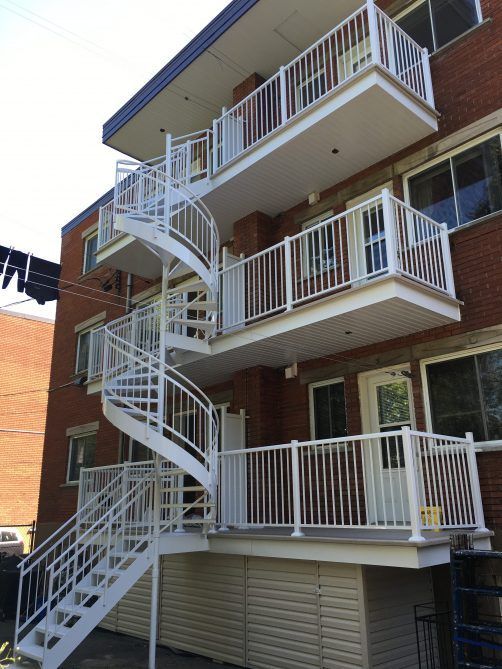 Escalier en colimaçon blanc et balcons sur un immeuble d'appartements en briques.
