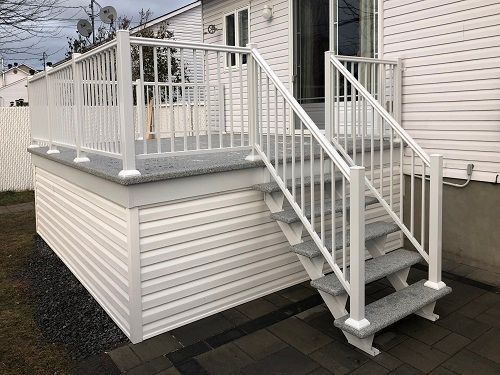 Terrasse blanche avec escalier, marches grises et rambarde blanche, adossée à une maison à l'extérieur blanc.