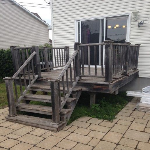 Terrasse en bois avec escalier, attenante à une maison avec portes coulissantes en verre ; aspect vieilli.