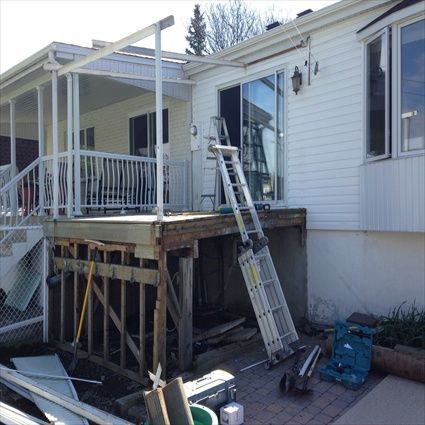 Terrasse en construction à côté d'une maison avec une porte-fenêtre coulissante et une échelle appuyée contre celle-ci.