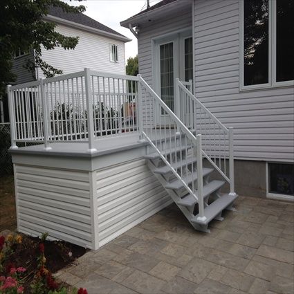 Terrasse et escalier blancs attenants à une maison au bardage blanc et au patio en pierre grise.