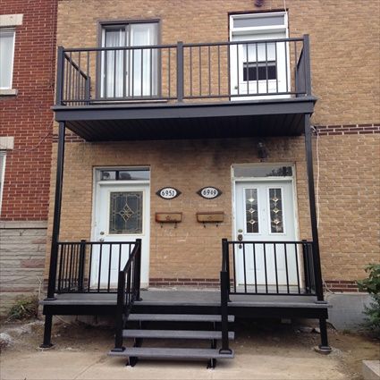 Extérieur d'un bâtiment de deux étages avec balcons, balustrades et escaliers noirs menant à des portes d'entrée blanches.