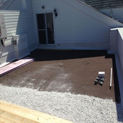 Toit-terrasse avec porte coulissante, gravier et surface brun foncé, travaux en cours.