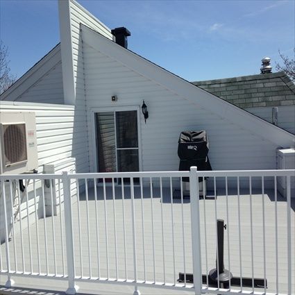 Terrasse blanche avec rambarde, maison avec toit en pente et porte coulissante, et grille noire.