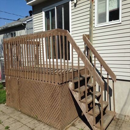 Terrasse en bois avec escalier menant à une porte coulissante en verre d'une maison au bardage gris.
