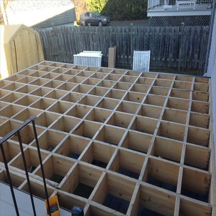 Construction d'une structure de terrasse en bois à l'arrière d'une maison, avec un motif en grille.