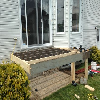 Construction d'une terrasse en cours à l'extérieur d'une maison avec une porte coulissante en verre.
