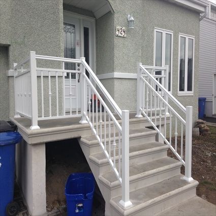 Rambarde blanche sur un escalier en béton menant à une maison à l'extérieur gris.