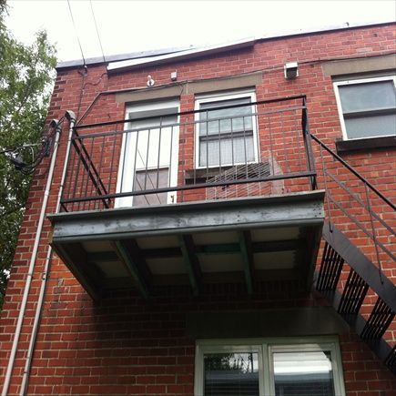Façade en briques avec balcon métallique et issue de secours. Fenêtres visibles.