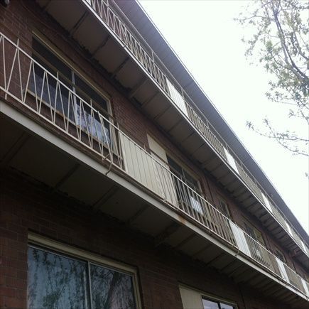 Vue en contre-plongée d'un immeuble d'appartements en briques avec balcons et balustrades blancs, sous un ciel nuageux.