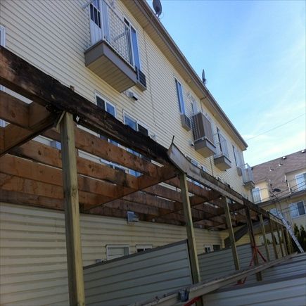 Auvent en bois en construction, fixé à un immeuble d'appartements beige équipé de climatiseurs.