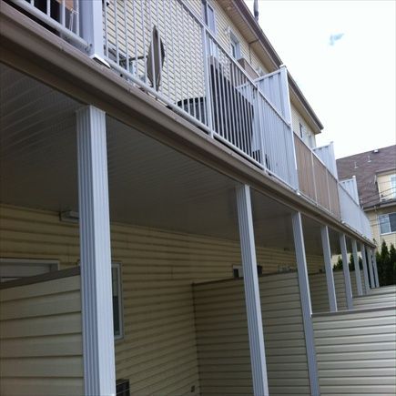 Bardage beige et rambarde blanche sur un bâtiment de deux étages avec balcon couvert et poutres de soutien.