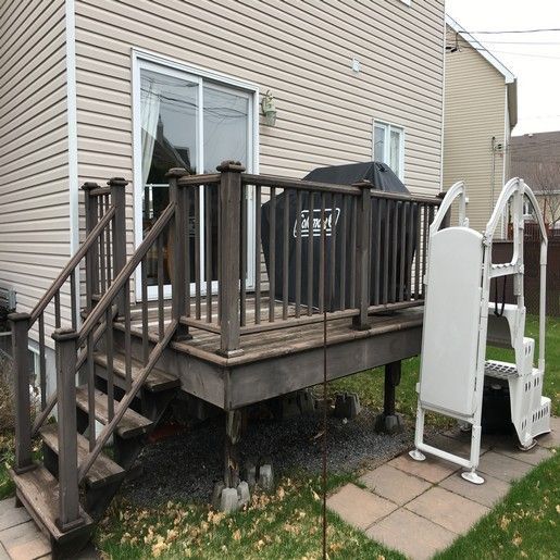 Terrasse en bois avec marches, barbecue et échelle de piscine, attenante à une maison avec porte-fenêtre coulissante.