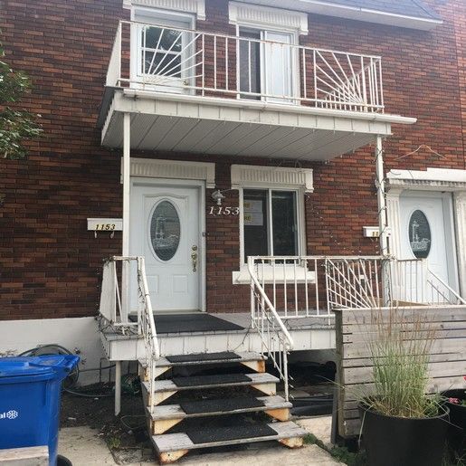 Un bâtiment en briques de deux étages avec des portes blanches, un porche et un balcon.
