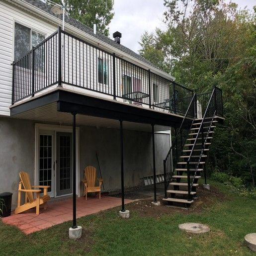Terrasse à deux niveaux avec balustrade et escalier noirs. Des portes extérieures donnent sur un patio en briques avec des chaises Adirondack.