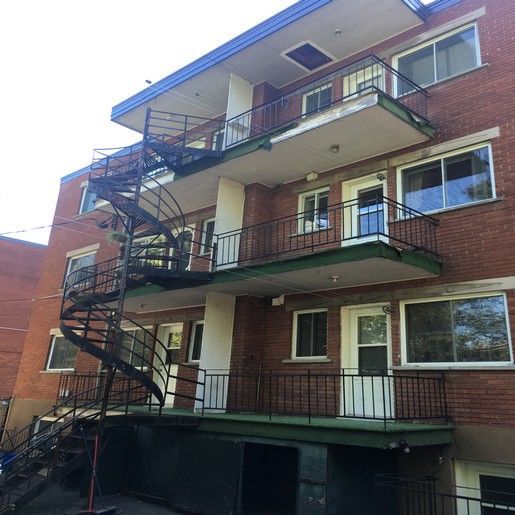 Immeuble d'appartements en briques avec escalier de secours en colimaçon. Balcons avec garde-corps noirs. Finitions bleues.