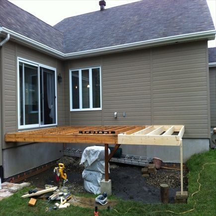 Construction d'une terrasse en cours ; structure en bois fixée à une maison avec porte-fenêtre coulissante et fenêtres.