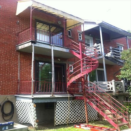 Bâtiment en briques rouges avec un escalier en colimaçon rouge menant à des balcons. Détail en treillis blanc.