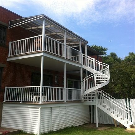 Terrasse sur deux niveaux avec un escalier en colimaçon sur un bâtiment en briques, peint en blanc.