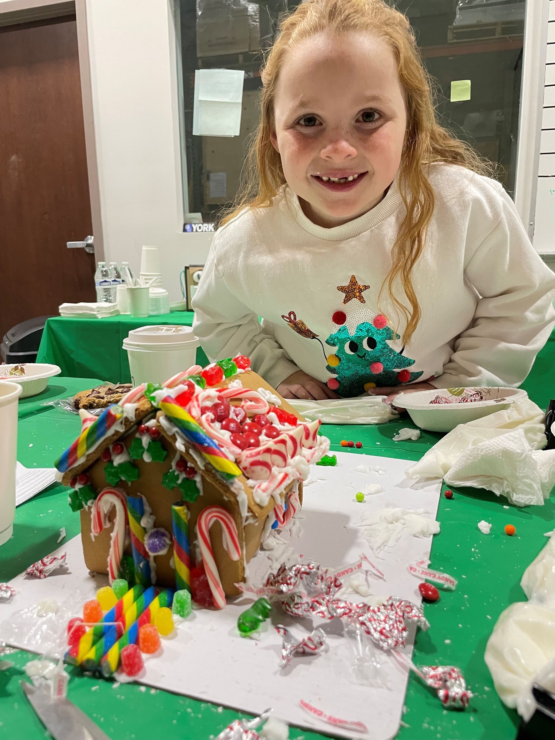 A little girl is sitting at a table with a gingerbread house on it