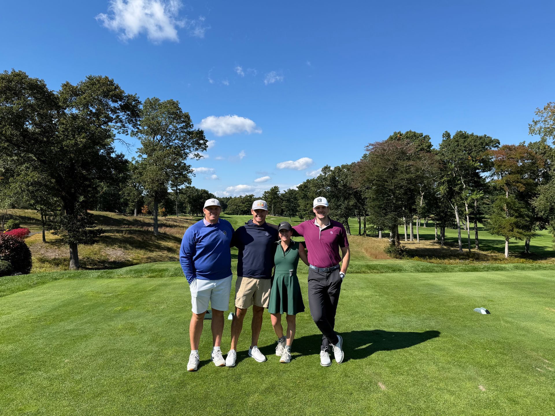 Four men standing on a golf course holding golf clubs