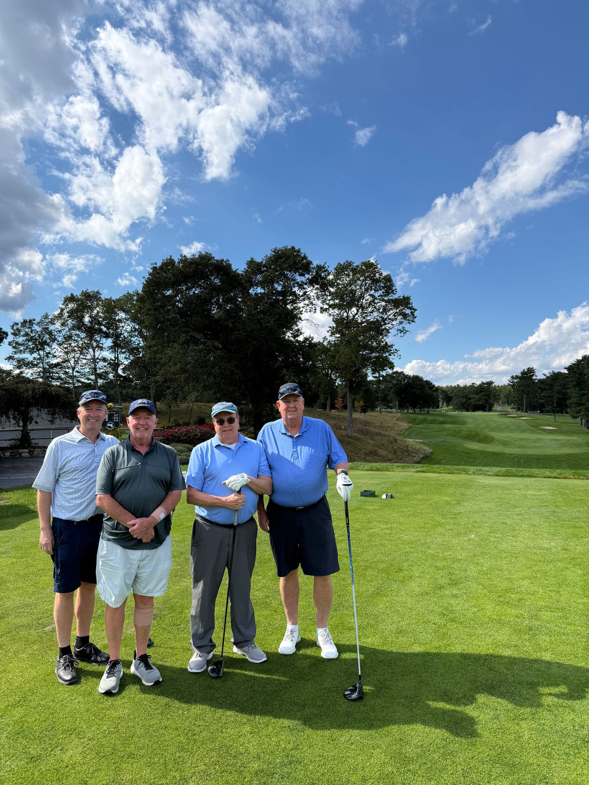 Four men are standing on a golf course holding golf clubs.