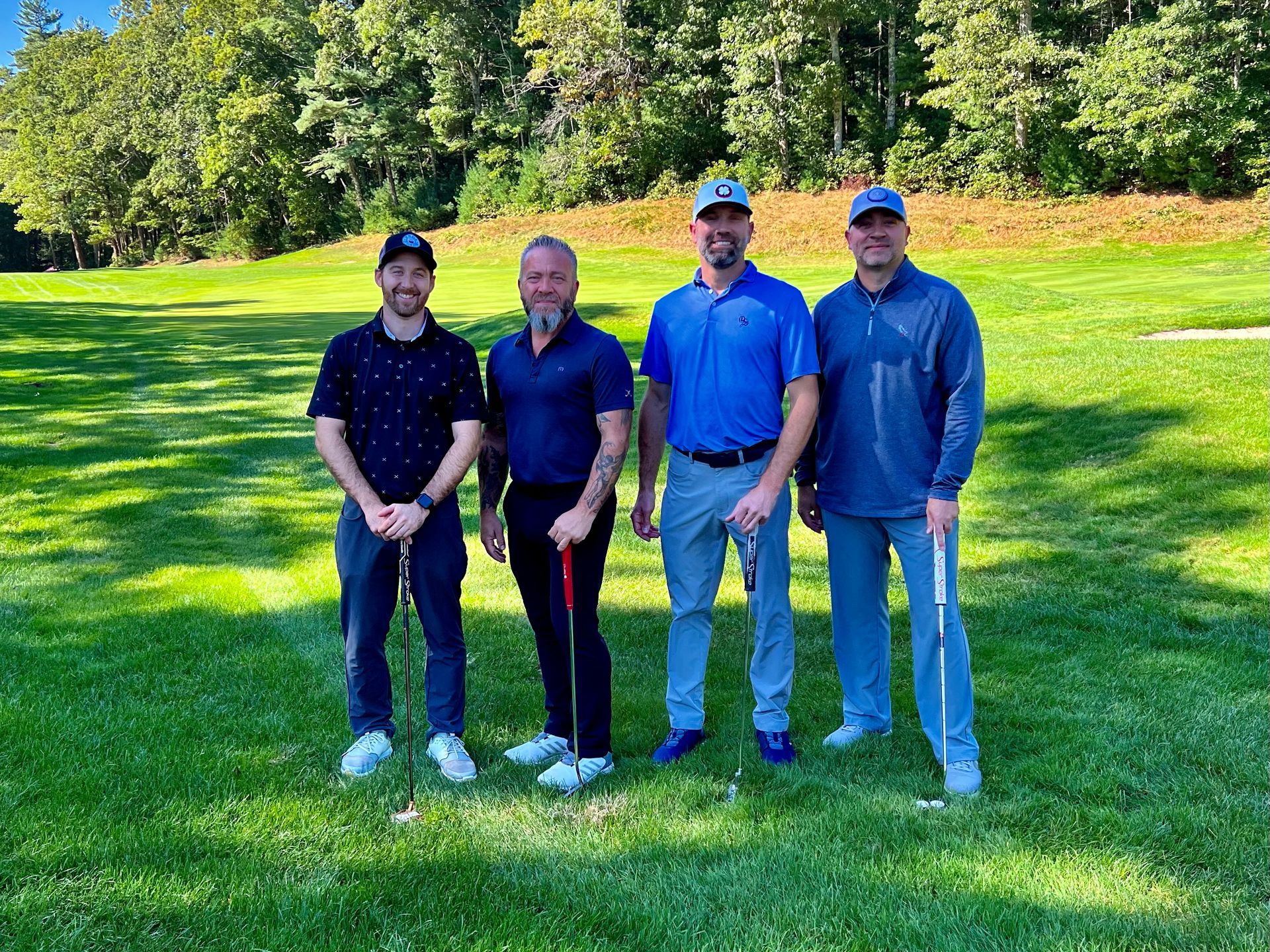 Four men are standing on a golf course holding golf clubs.