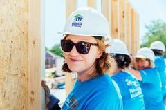 A woman wearing a hard hat and sunglasses is standing next to a group of construction workers.