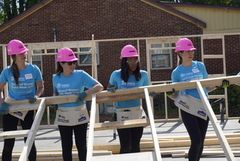 A group of women wearing hard hats and aprons are carrying wood.