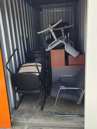 Storage unit cluttered with stacked chairs and a tipped office chair in a narrow corridor