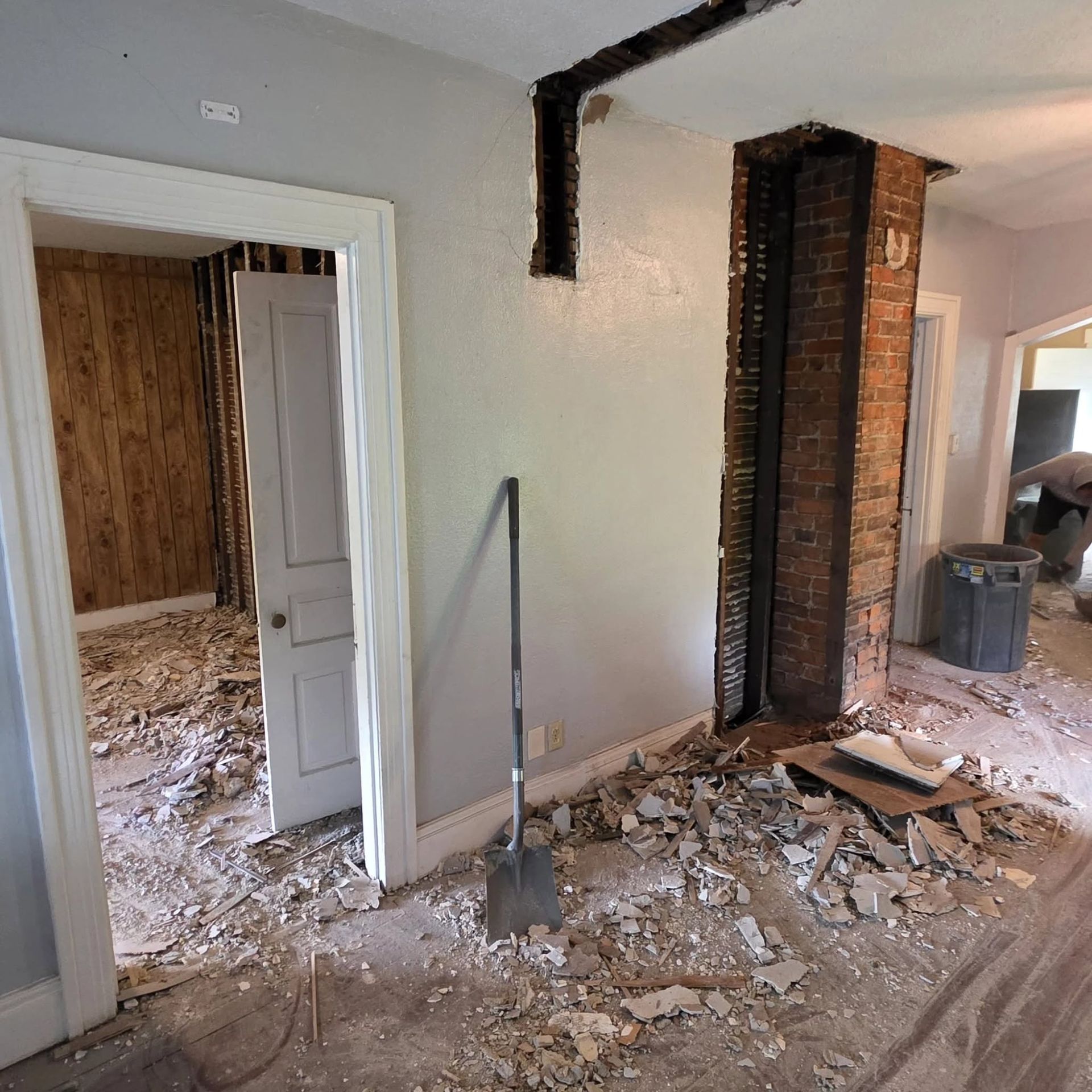 Renovated interior with exposed brick, debris on the floor, and open doorways in a damaged room