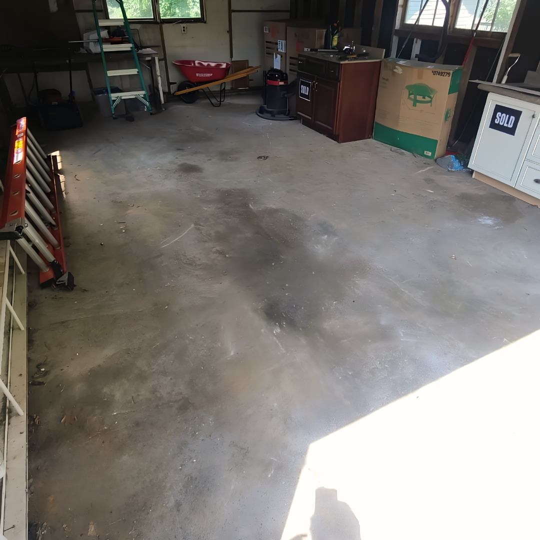 Empty garage with concrete floor, shelves, cabinets, boxes, and a red bicycle near the back wall.
