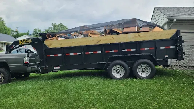 Collapsed deck and stairs beside a house, with a small excavator and scattered debris in the yard.