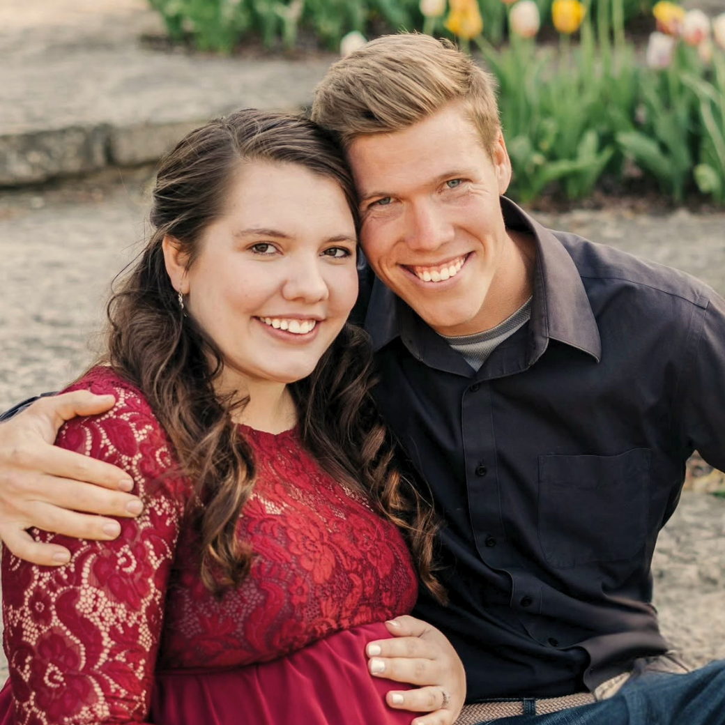 Smiling couple seated outdoors, embracing in a garden path setting.