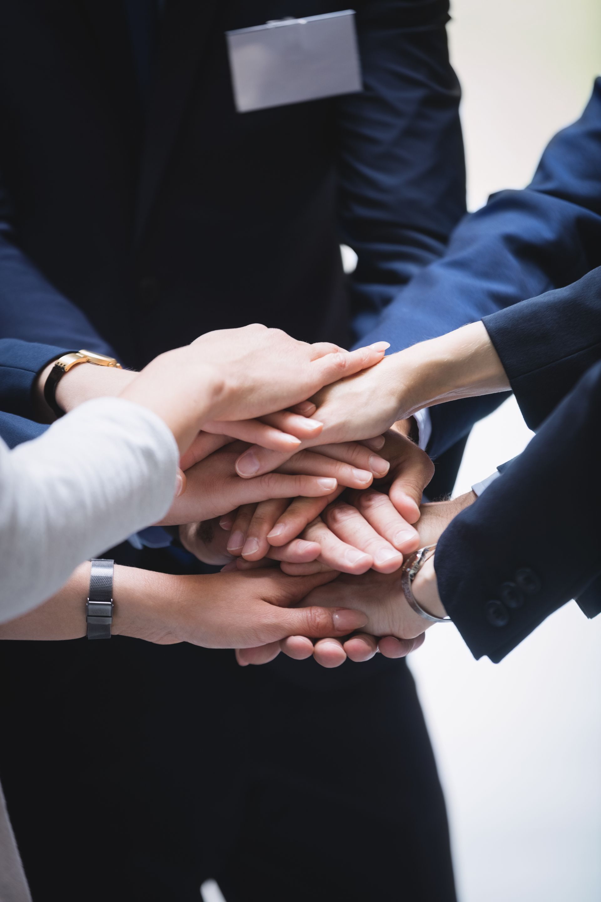 Stacked hands in a team huddle, sleeves in black, white, and navy suits.