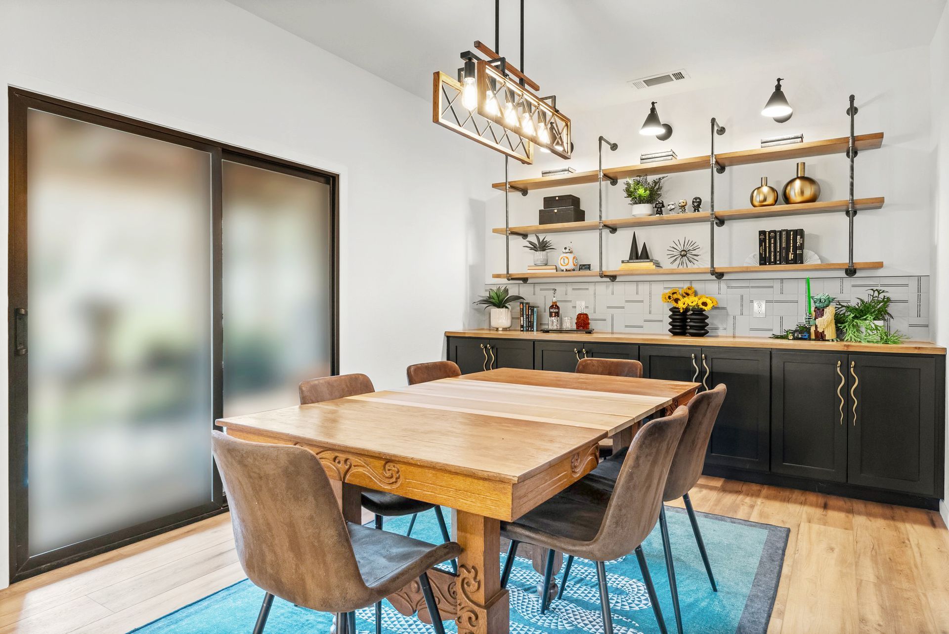 Modern dining room with wooden table, upholstered chairs, black sideboard, and wall shelves near frosted sliding doors