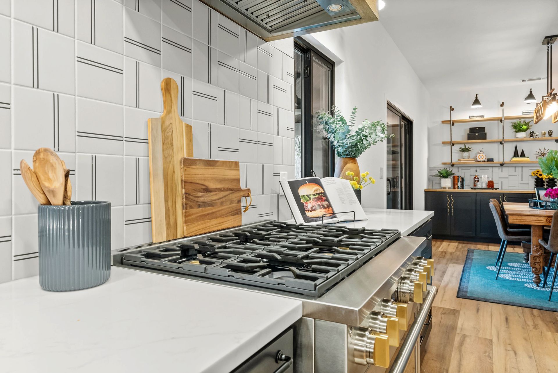 Modern kitchen with white cabinets, gas cooktop, wooden cutting boards, and a blue rug in the dining area