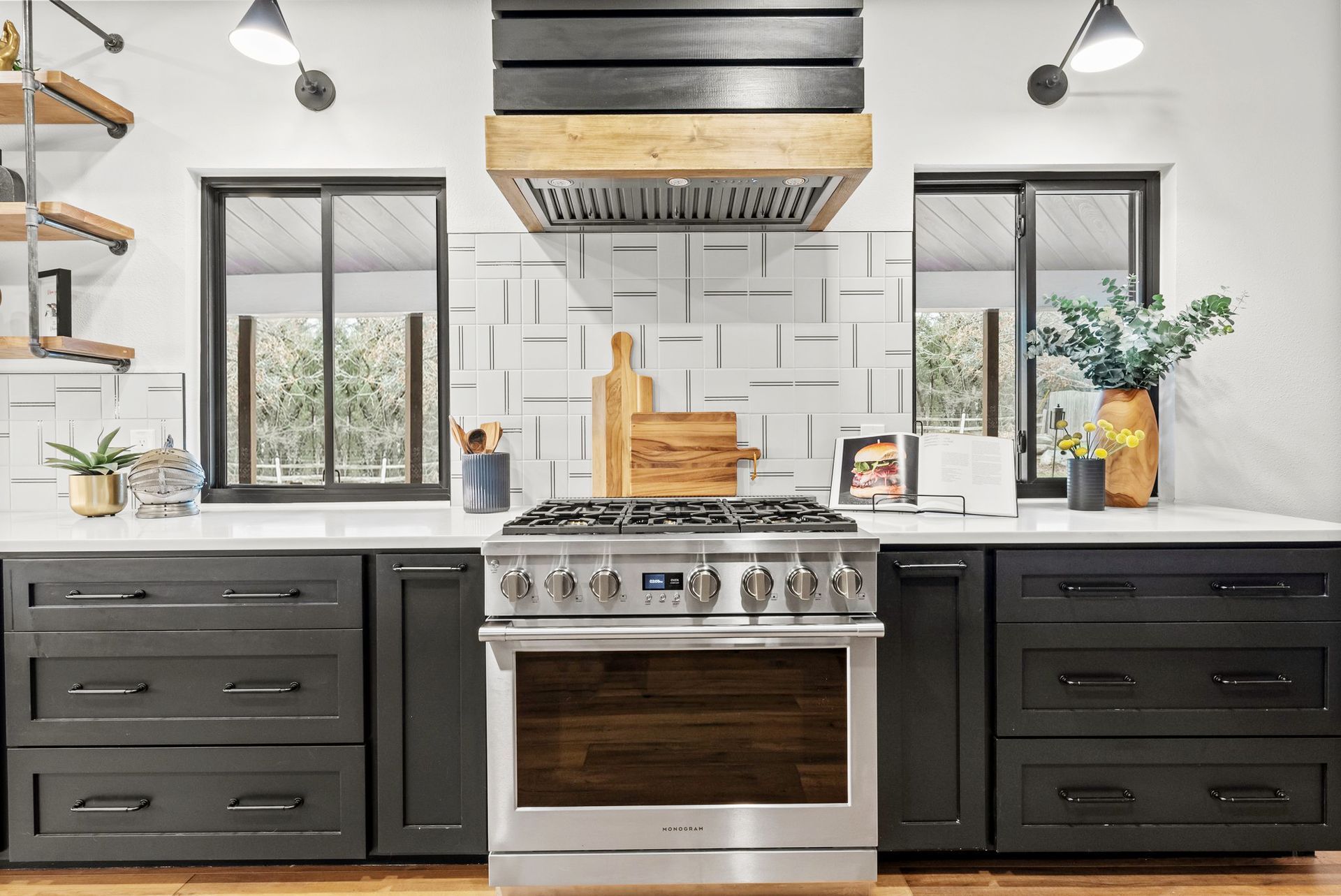 Modern kitchen with black cabinets, stainless range, white tile backsplash, and two windows