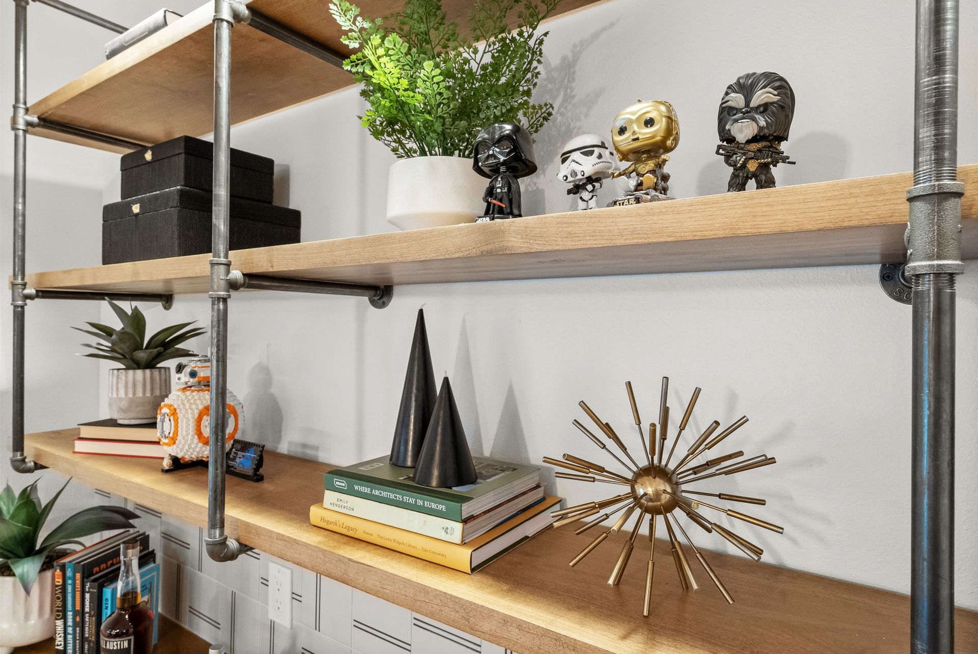 Wooden shelves with books, plants, figurines, and gold sunburst decor against a white wall