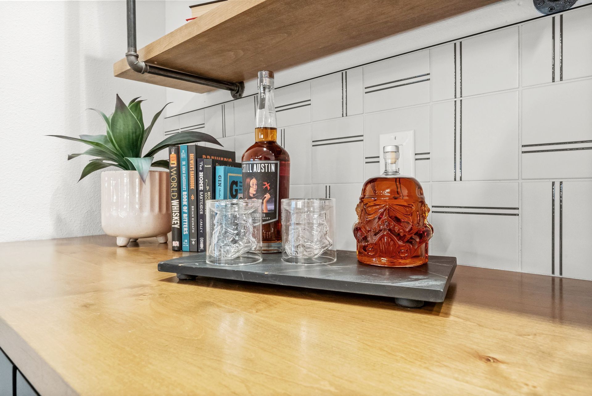 Wooden shelf with whiskey bottles and glasses on a tray beside a potted plant
