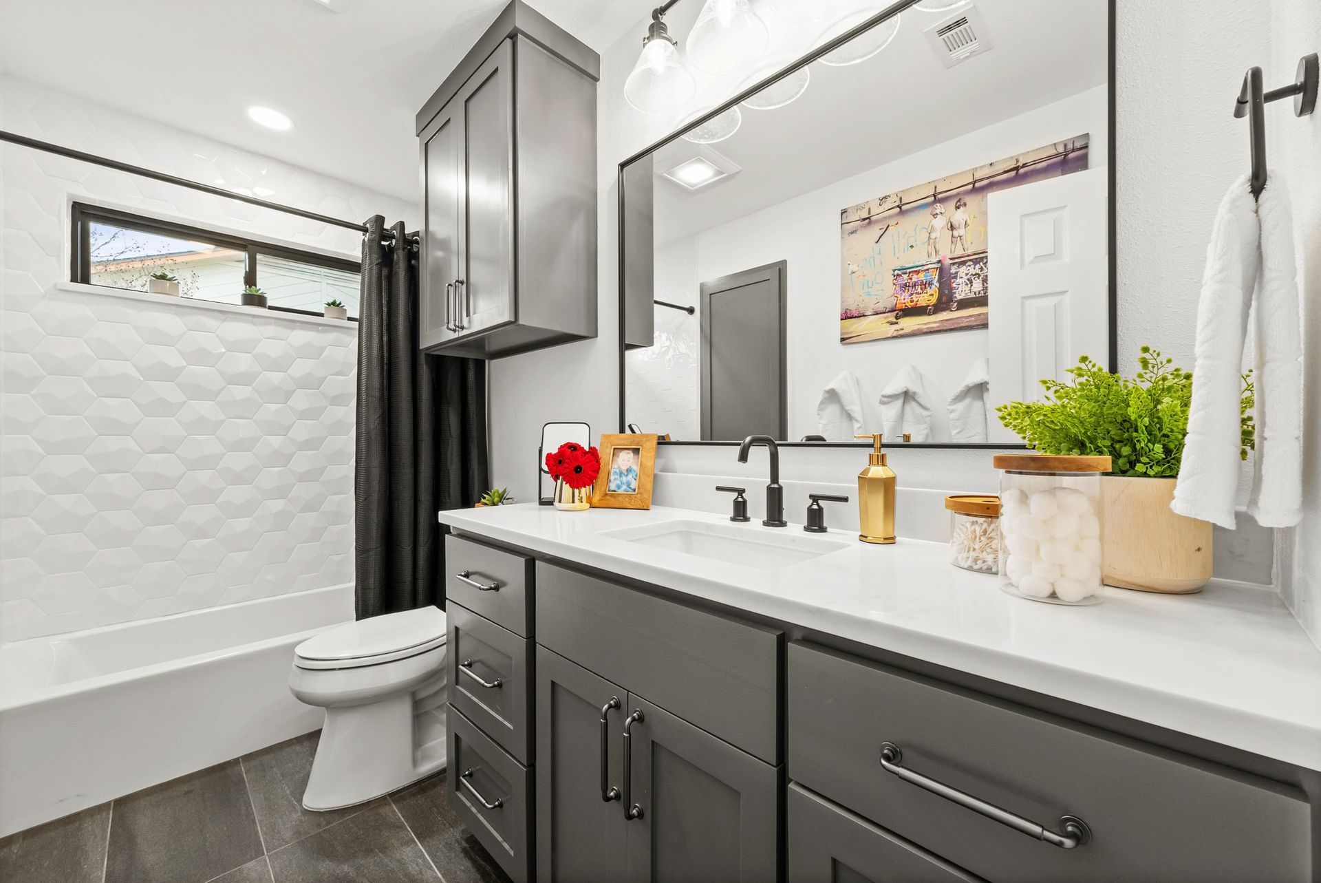 Modern bathroom with gray vanity, white sink, large mirror, and tiled shower behind a curtain
