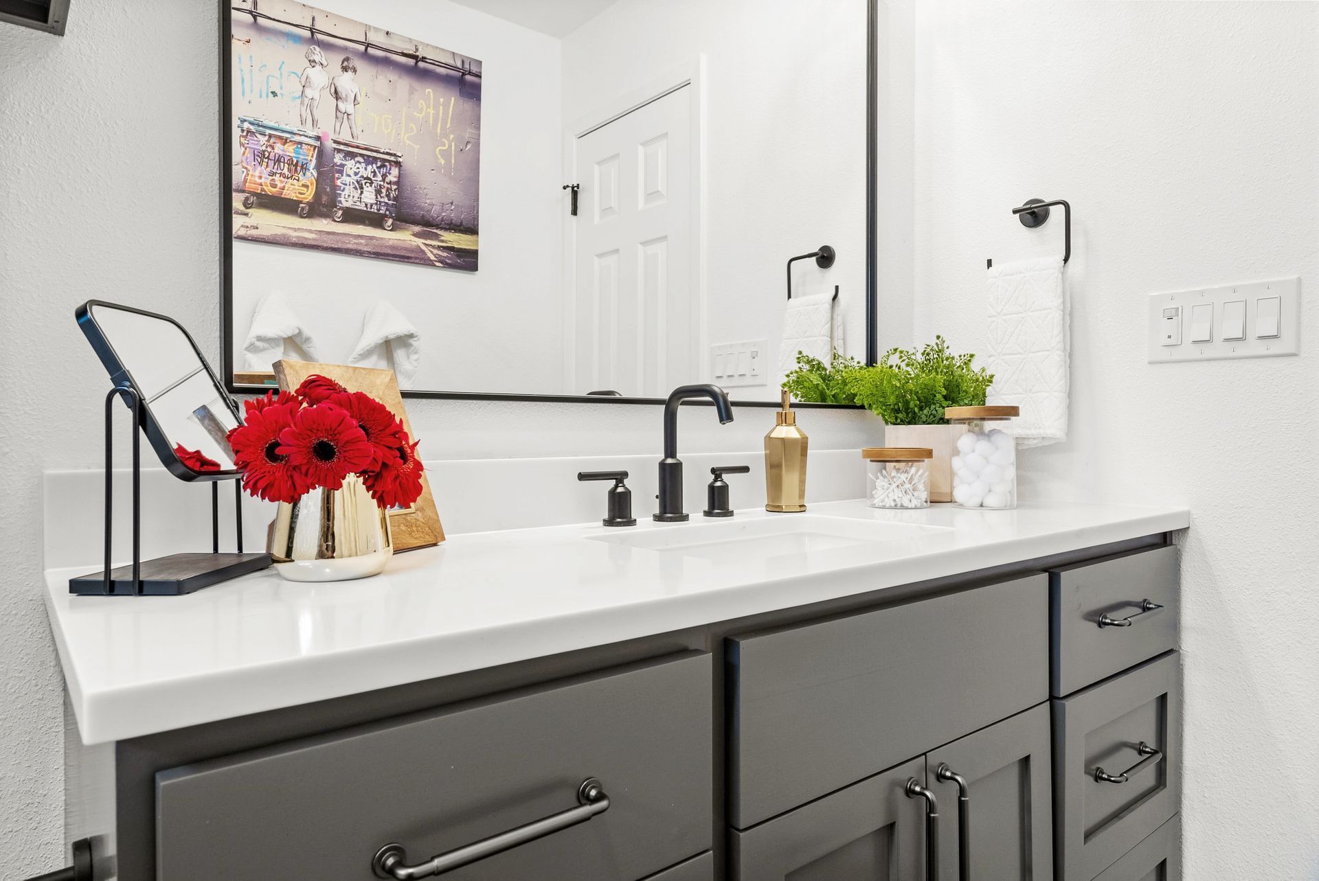Modern bathroom vanity with white countertop, black fixtures, flowers, and green potted plants