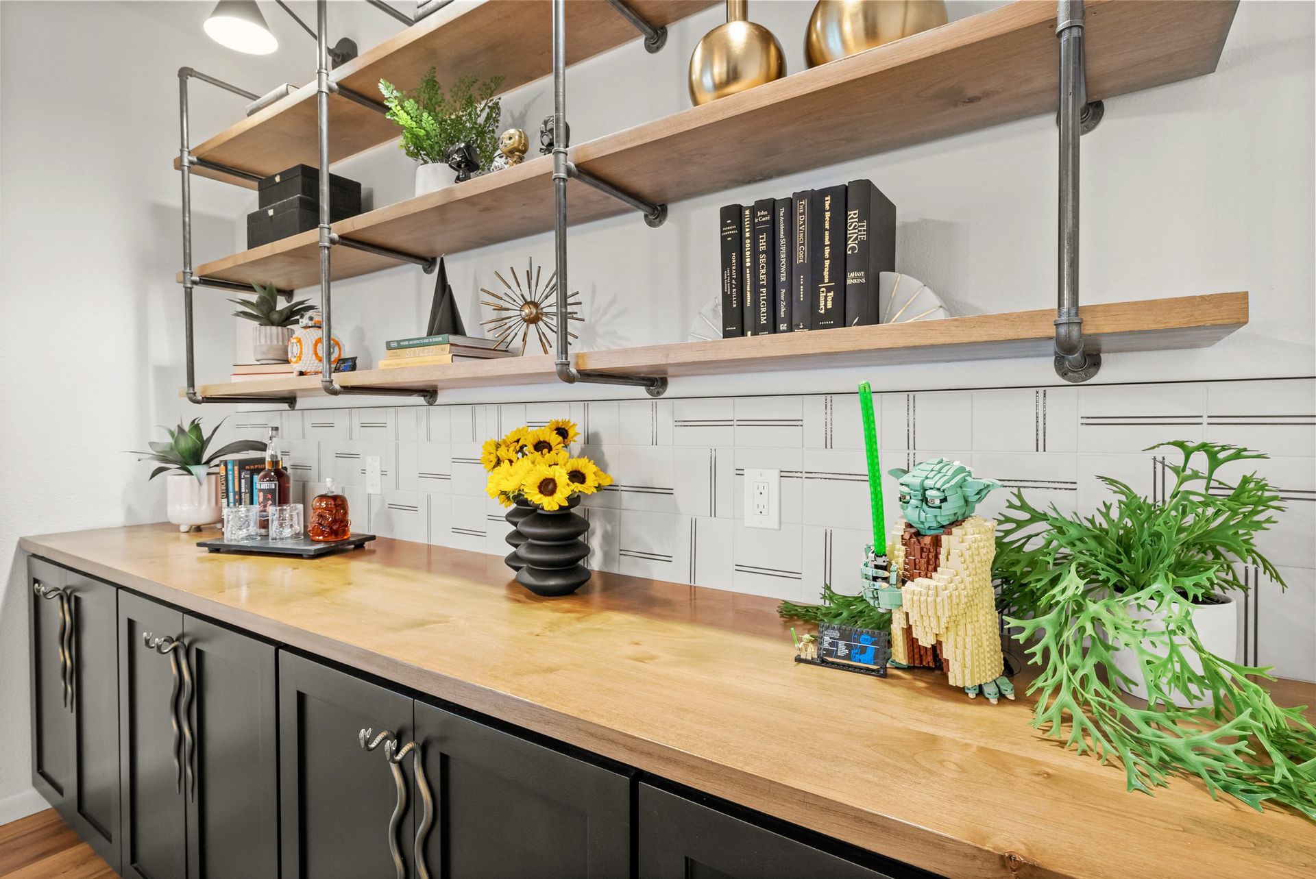 Modern kitchen with wood shelves, black cabinets, and a countertop decorated with flowers and plants
