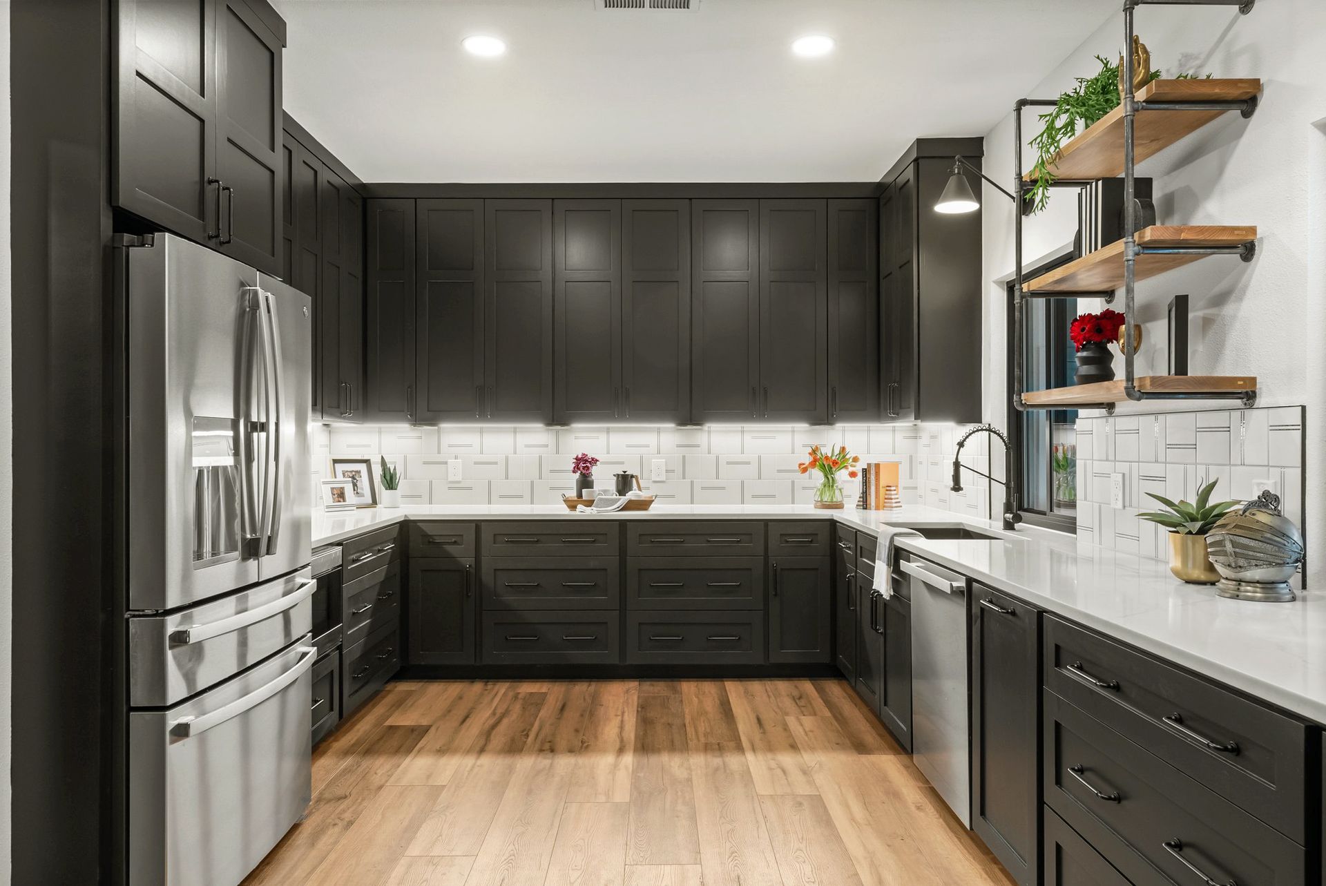 Modern kitchen with dark cabinets, stainless steel appliances, white backsplash, and wood floors
