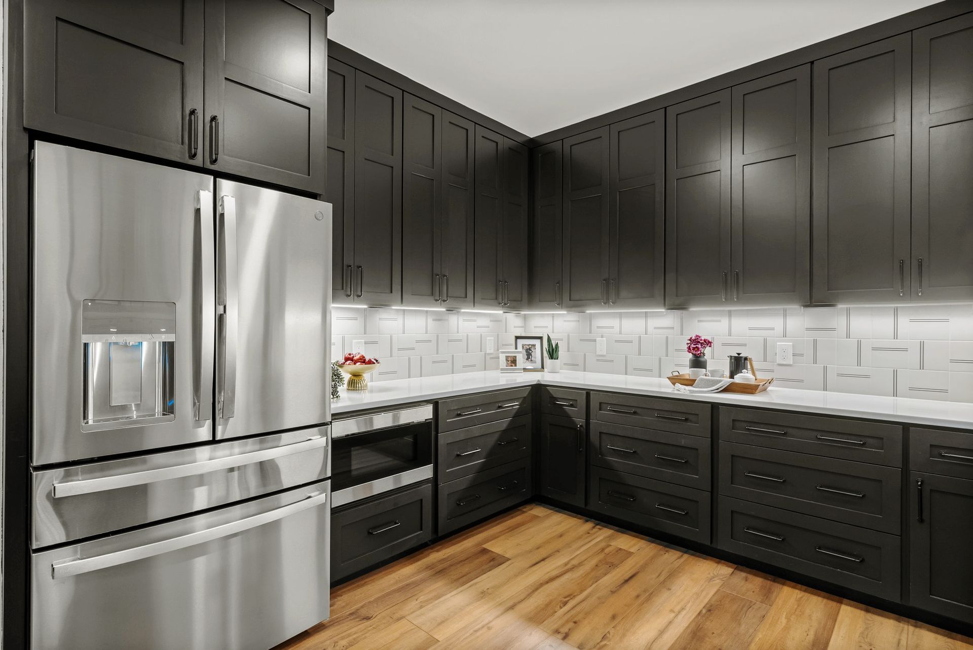 Modern kitchen with dark cabinets, stainless steel appliances, white subway tile backsplash, and wood flooring