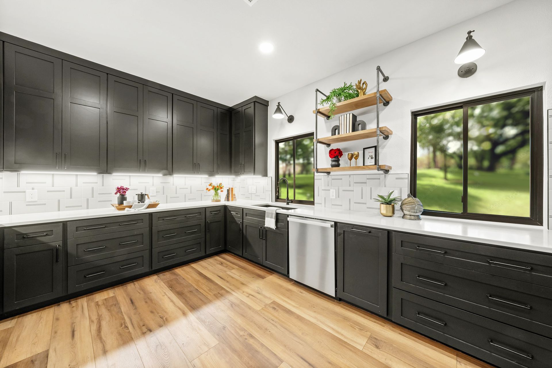 Bright modern kitchen with black cabinets, wood floors, white subway tile, and a large window overlooking greenery