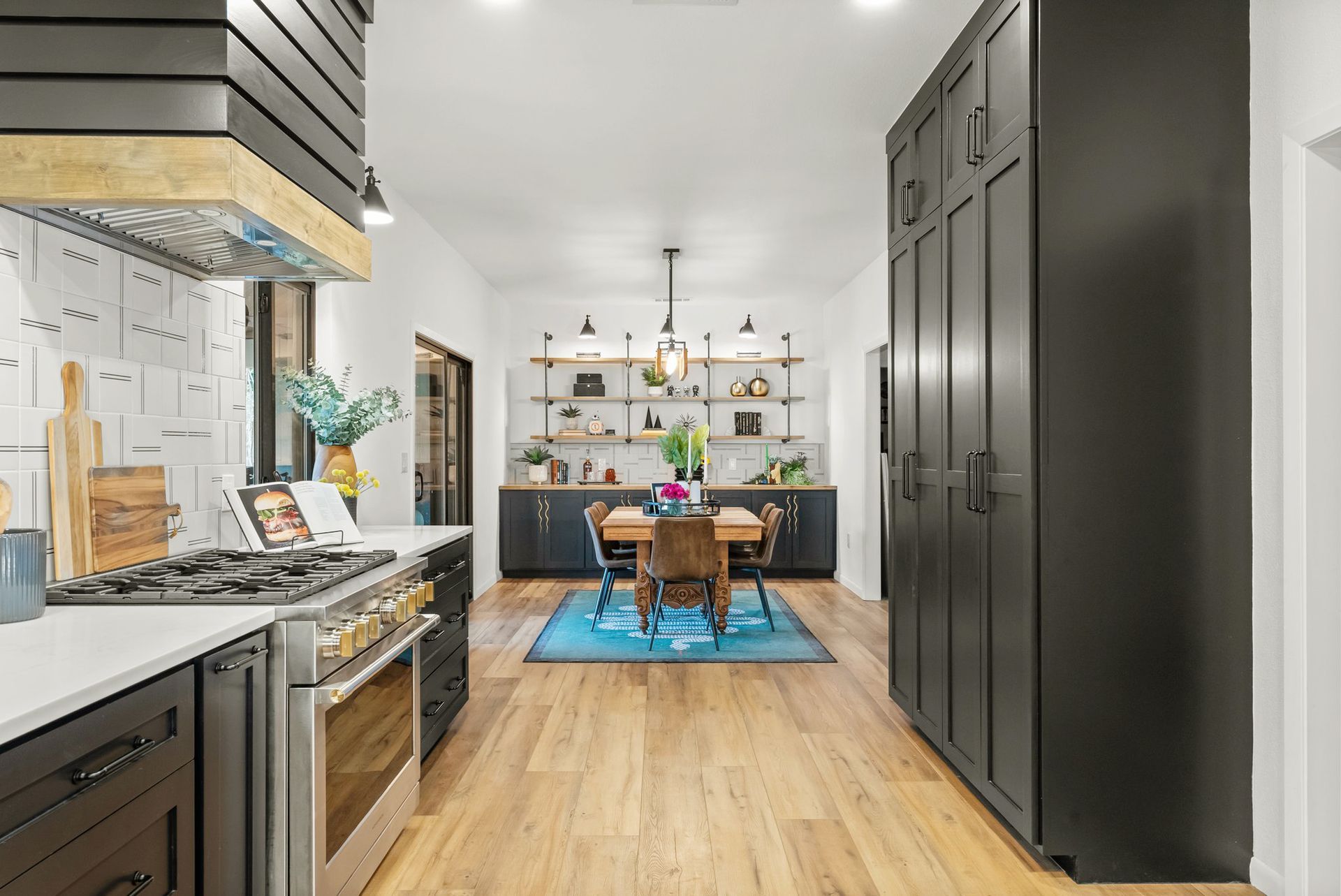 Modern kitchen with dark cabinets, wooden floor, and a dining table on a blue rug in the background