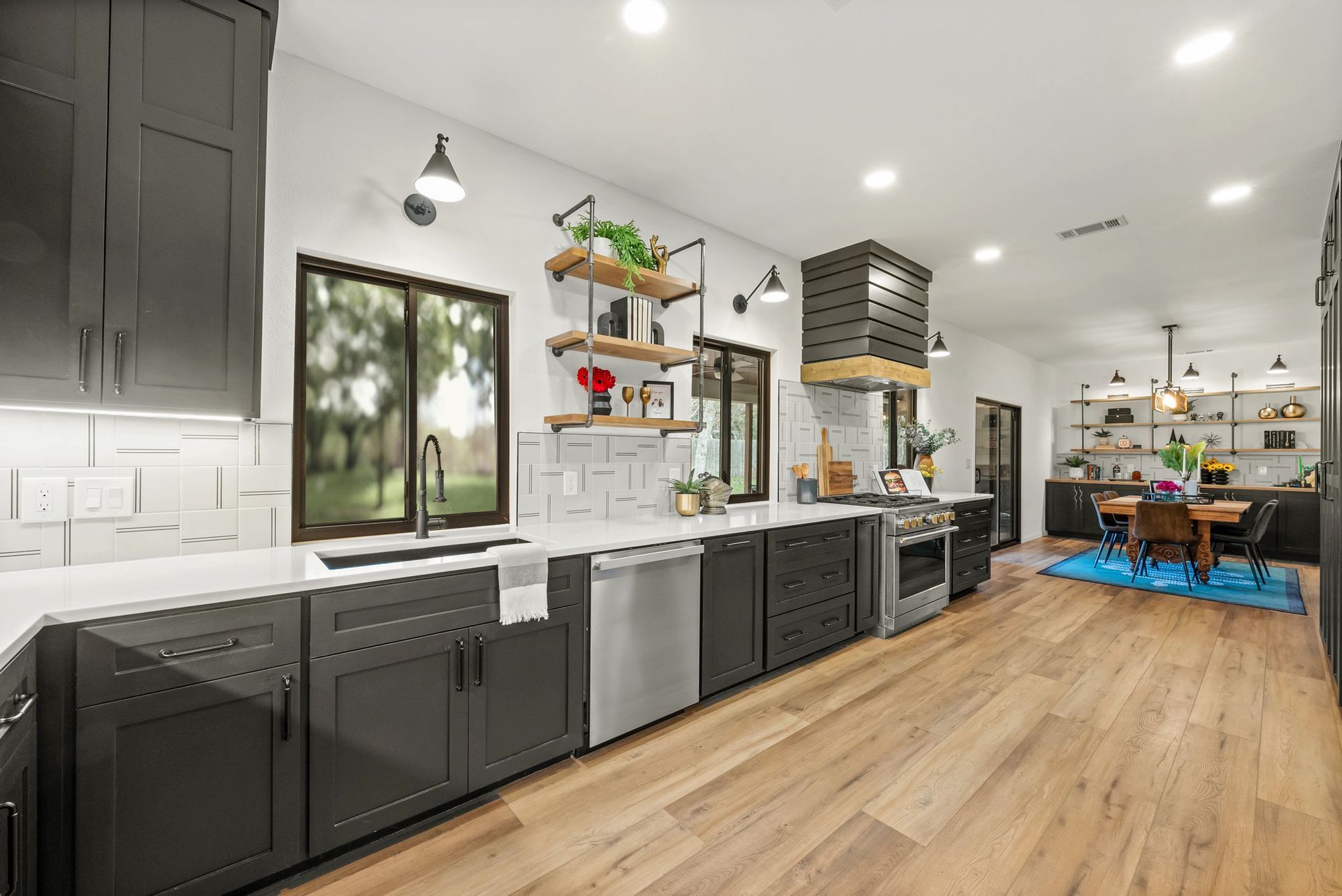 Modern kitchen with dark cabinets, white countertops, wood floors, and a dining area by large windows