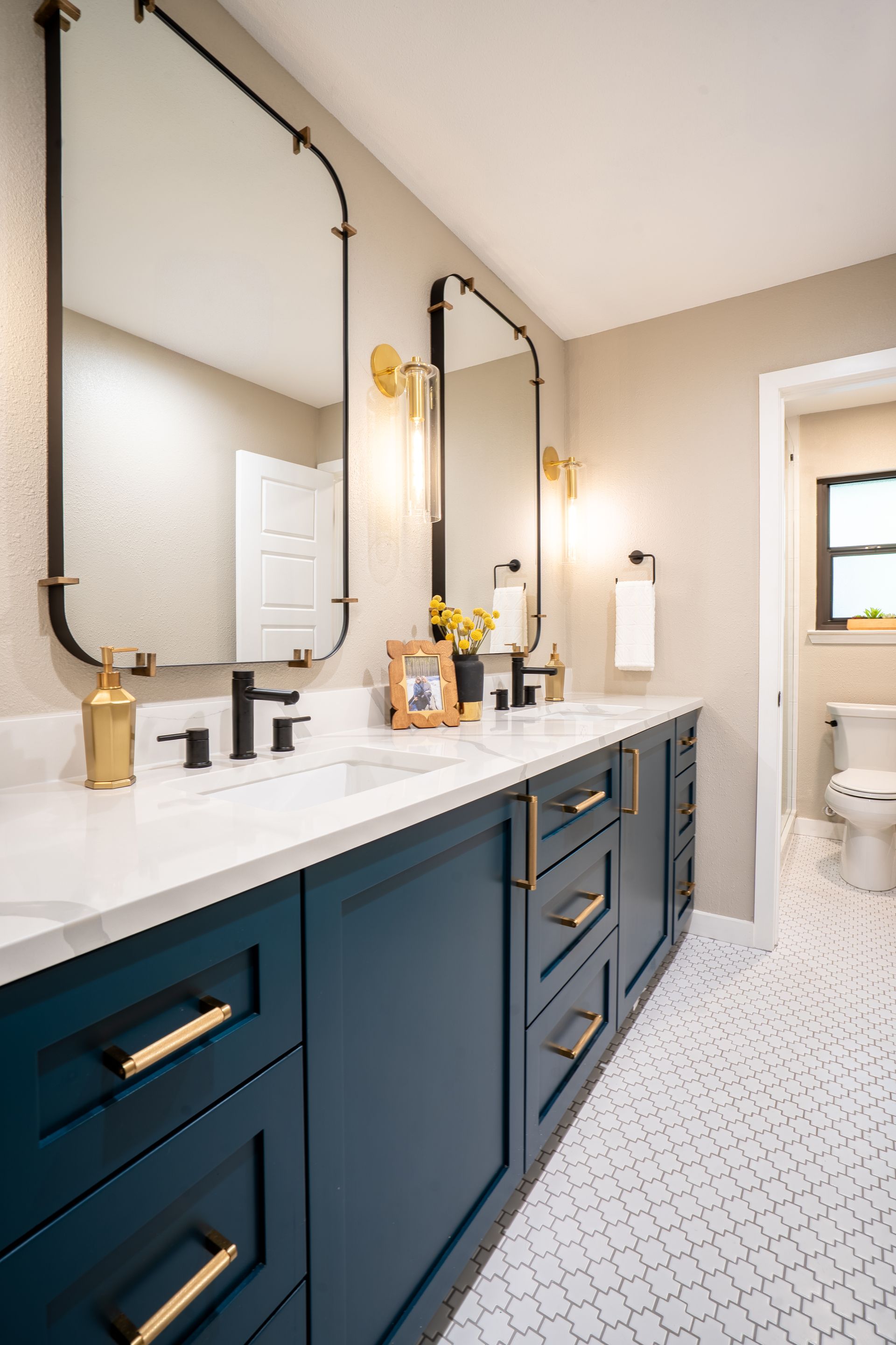 Modern bathroom vanity with navy cabinets, white countertop, gold fixtures, and mirror sconces